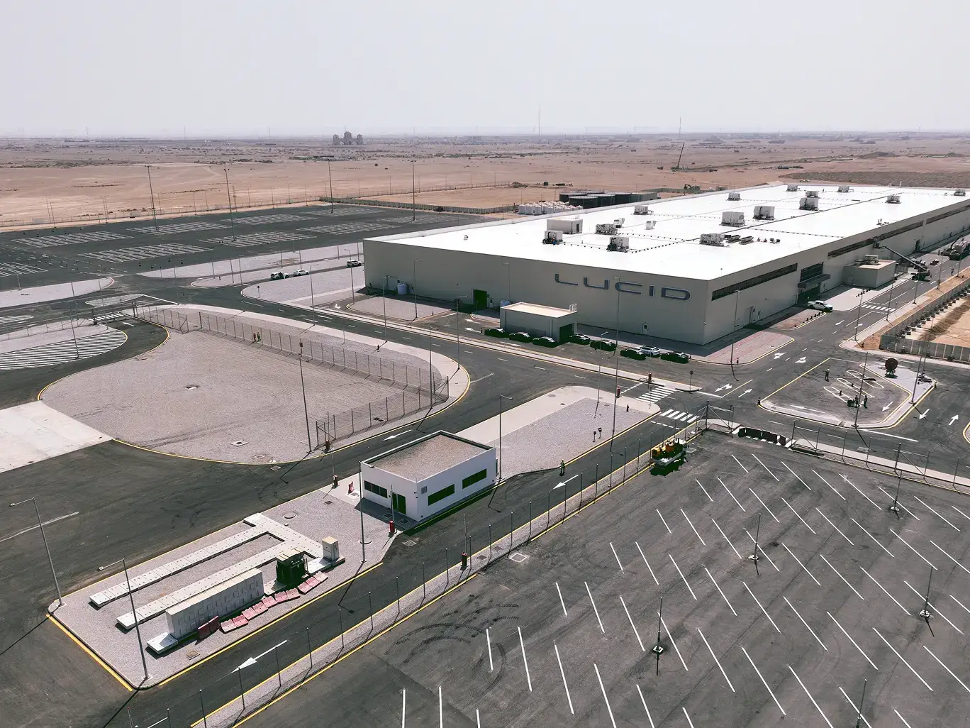 Aerial view of Lucid Motors' manufacturing facility in a desert landscape, featuring a large white building with parking lots.