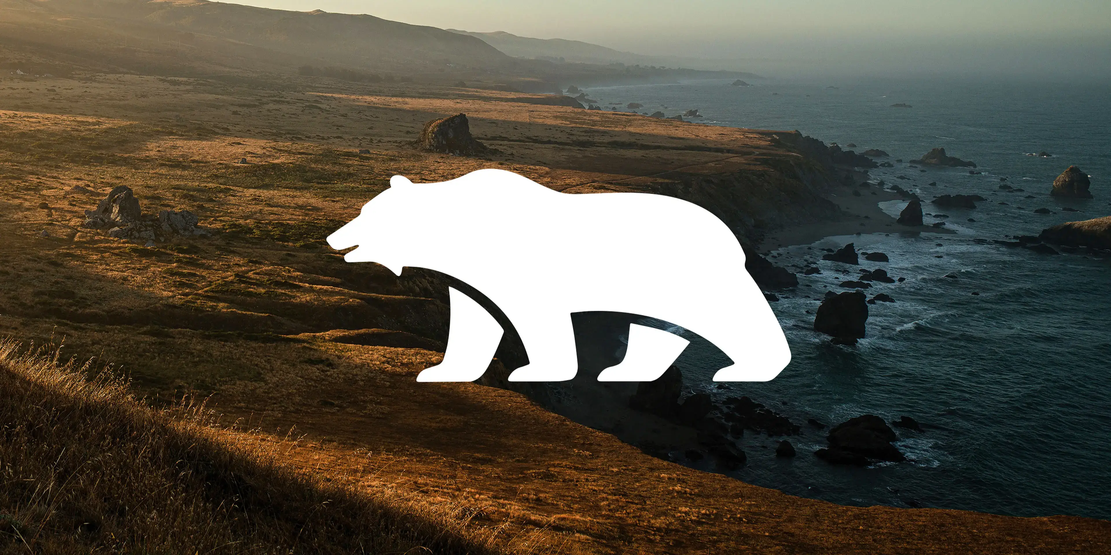 White bear silhouette overlaid on coastal landscape with golden hills meeting rocky shoreline and misty ocean at sunset.