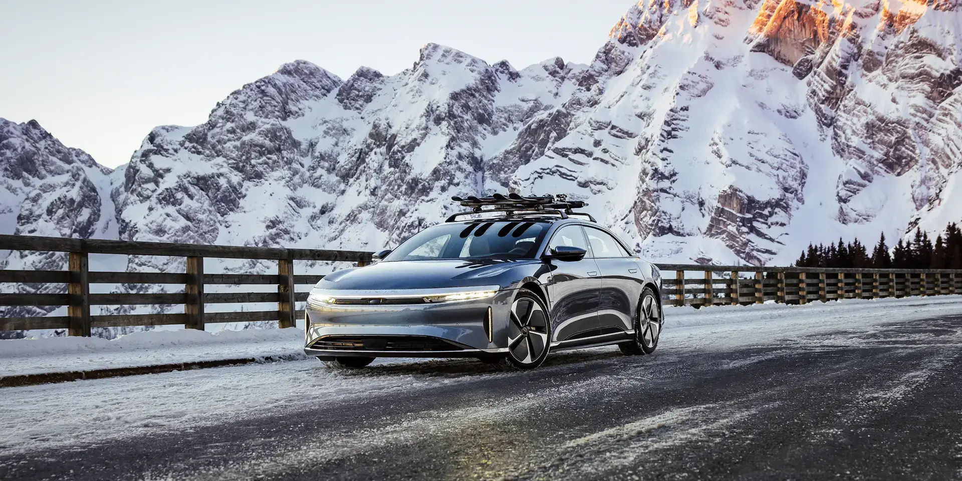 Une Lucid Air équipée d'un porte-skis et circulant sur une route de montagne, avec des pics enneigés spectaculaires en arrière-plan.