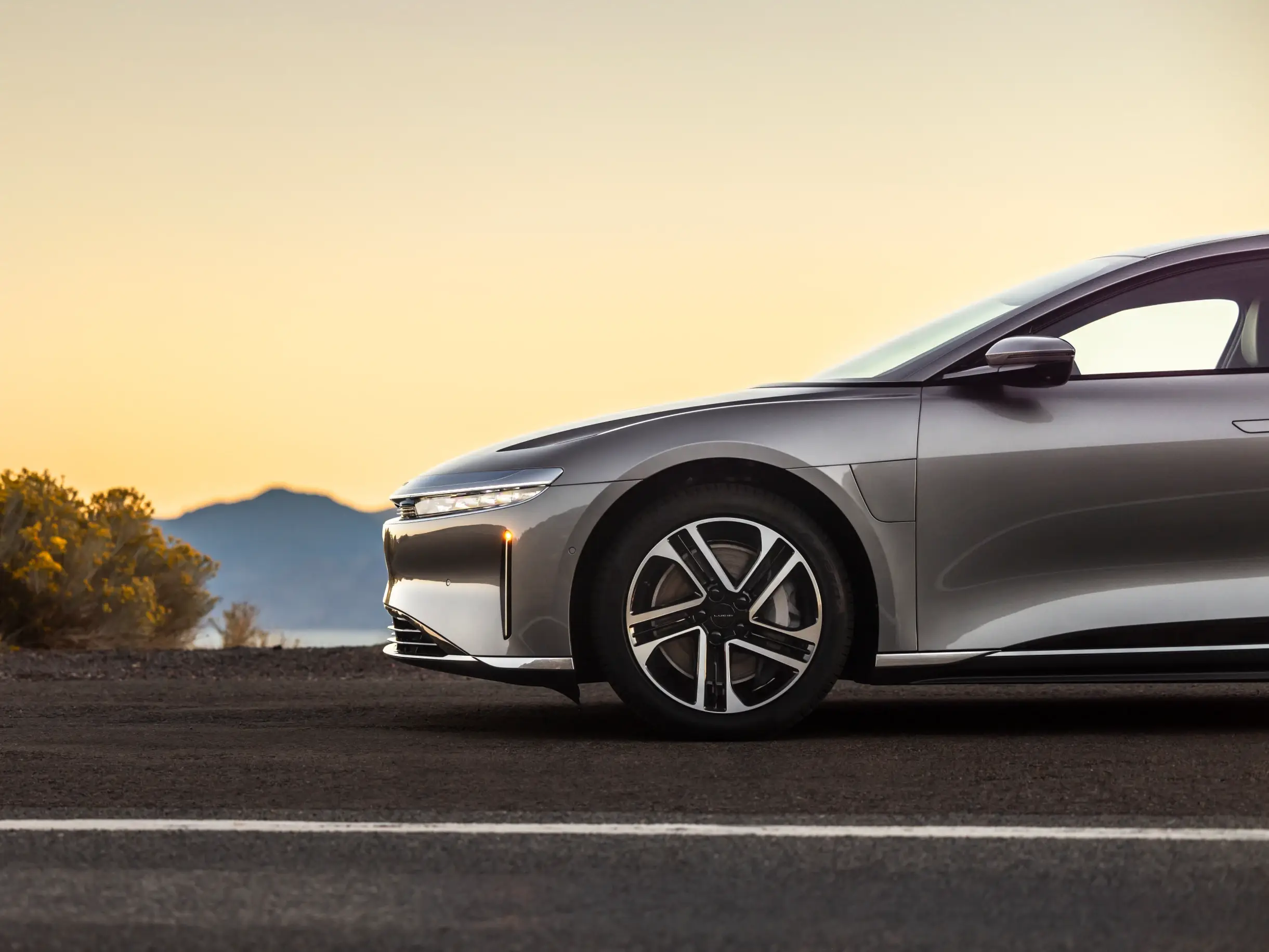 L’avant d’une Lucid Air garée au coucher du soleil, avec des montagnes au loin.
