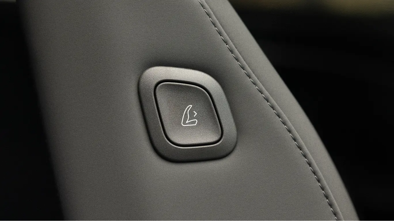 Grey leather car seat with a square button featuring a seat folding icon, part of vehicle’s interior controls.