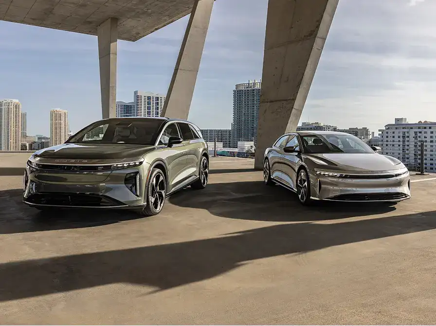Two sleek Lucid electric vehicles parked under modern concrete architecture with city skyline in background.