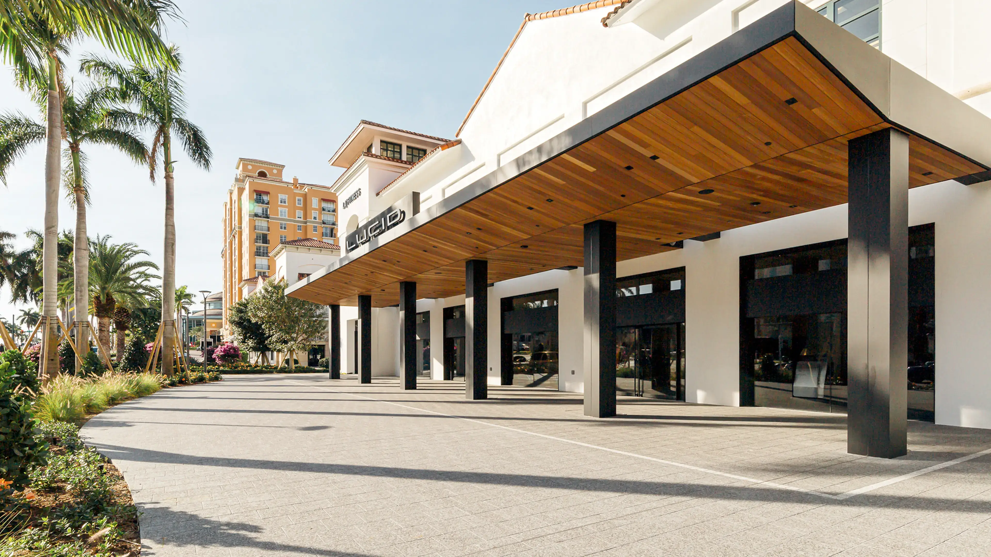 Modern Lucid storefront with wooden overhang and black columns, adjacent to a tall orange apartment building.