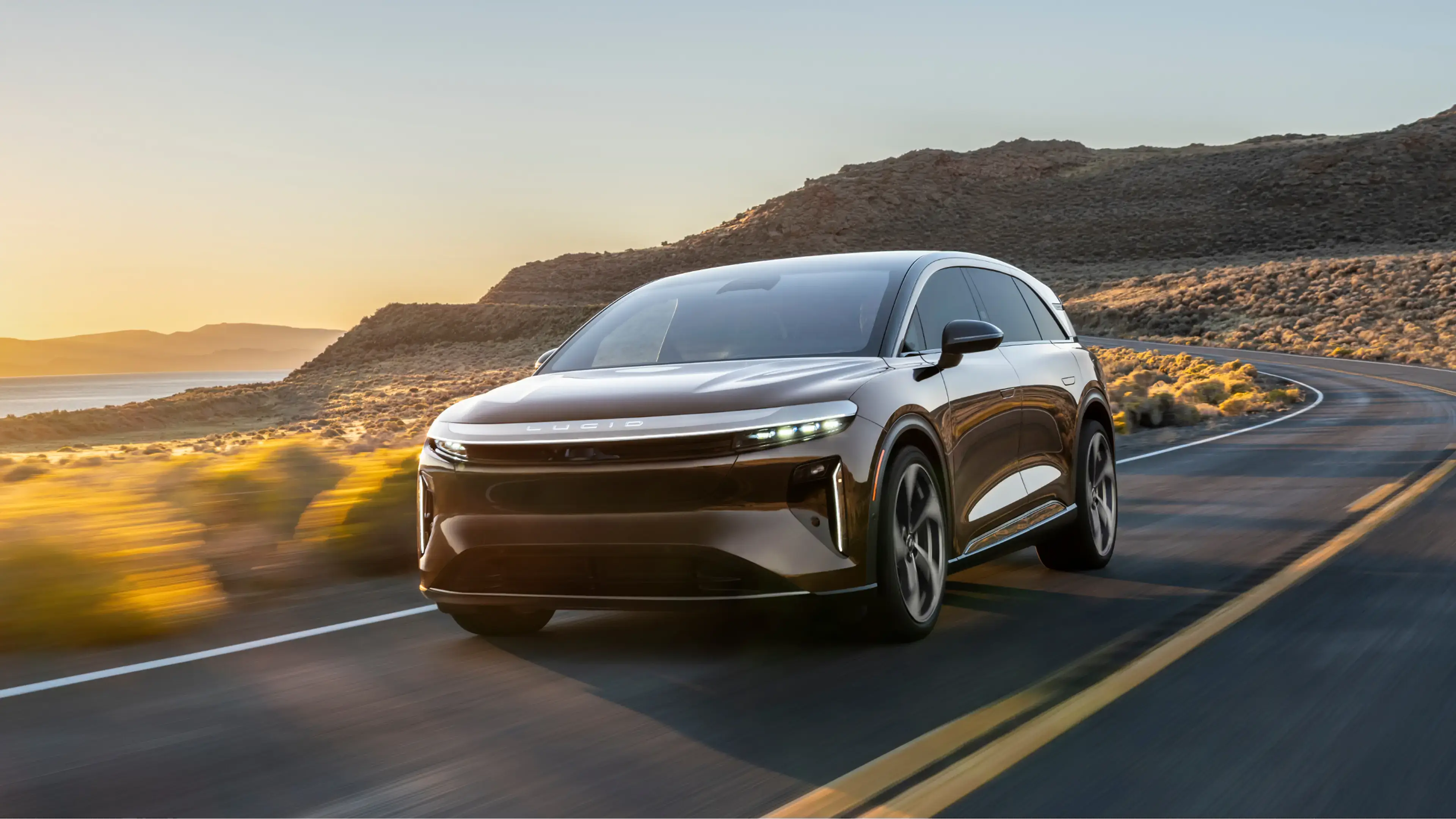 Lucid Gravity driving on a desert highway at sunset, with mountains in the background and golden light.