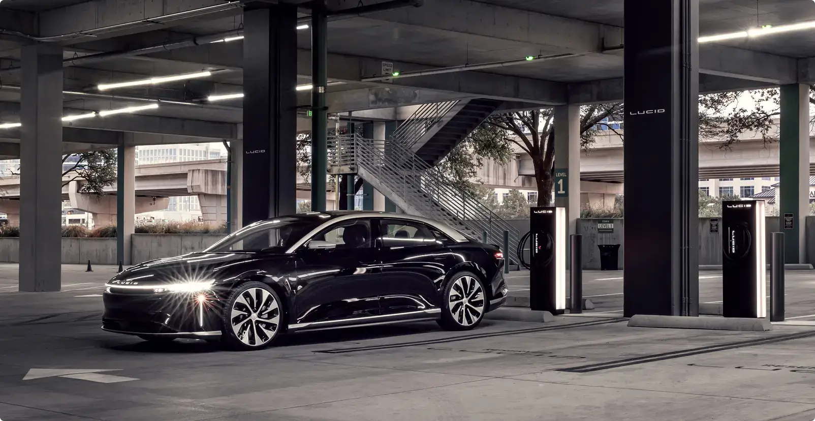 Lucid electric vehicle parked at a charging station in a modern concrete parking structure with ambient lighting.
