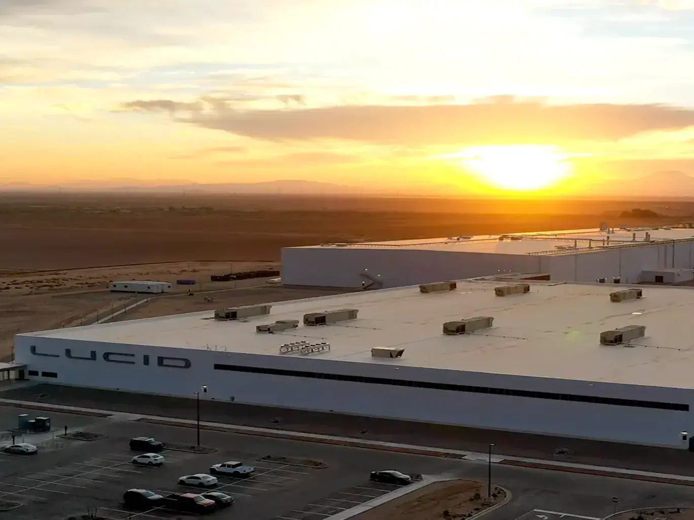 Aerial view of Lucid Motors' large white manufacturing facility in a desert landscape at sunset with golden skies.
