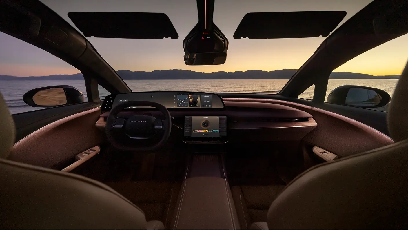Lucid Gravity interior with digital dashboard and touchscreens, overlooking a sunset over water with mountains in distance.
