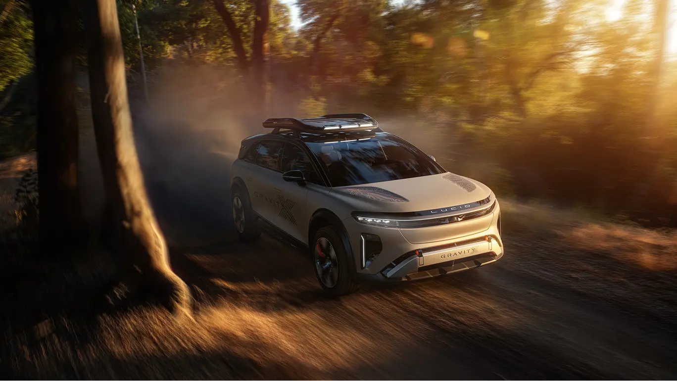 White Lucid Gravity SUV driving on a forest trail with golden sunlight filtering through trees, creating a misty atmosphere.