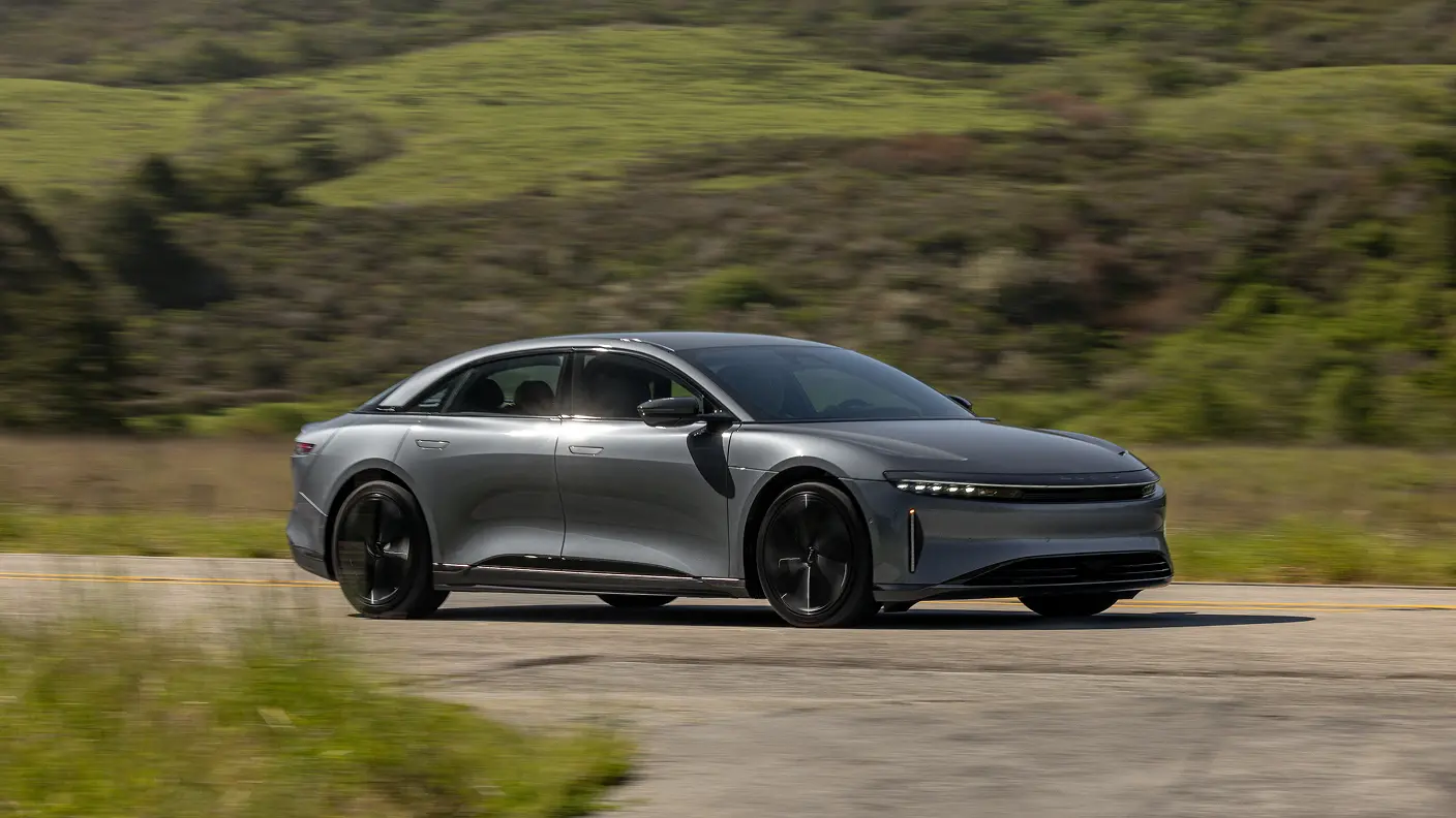 Lucid Air sedan driving on a rural road with green rolling hills in the background.
