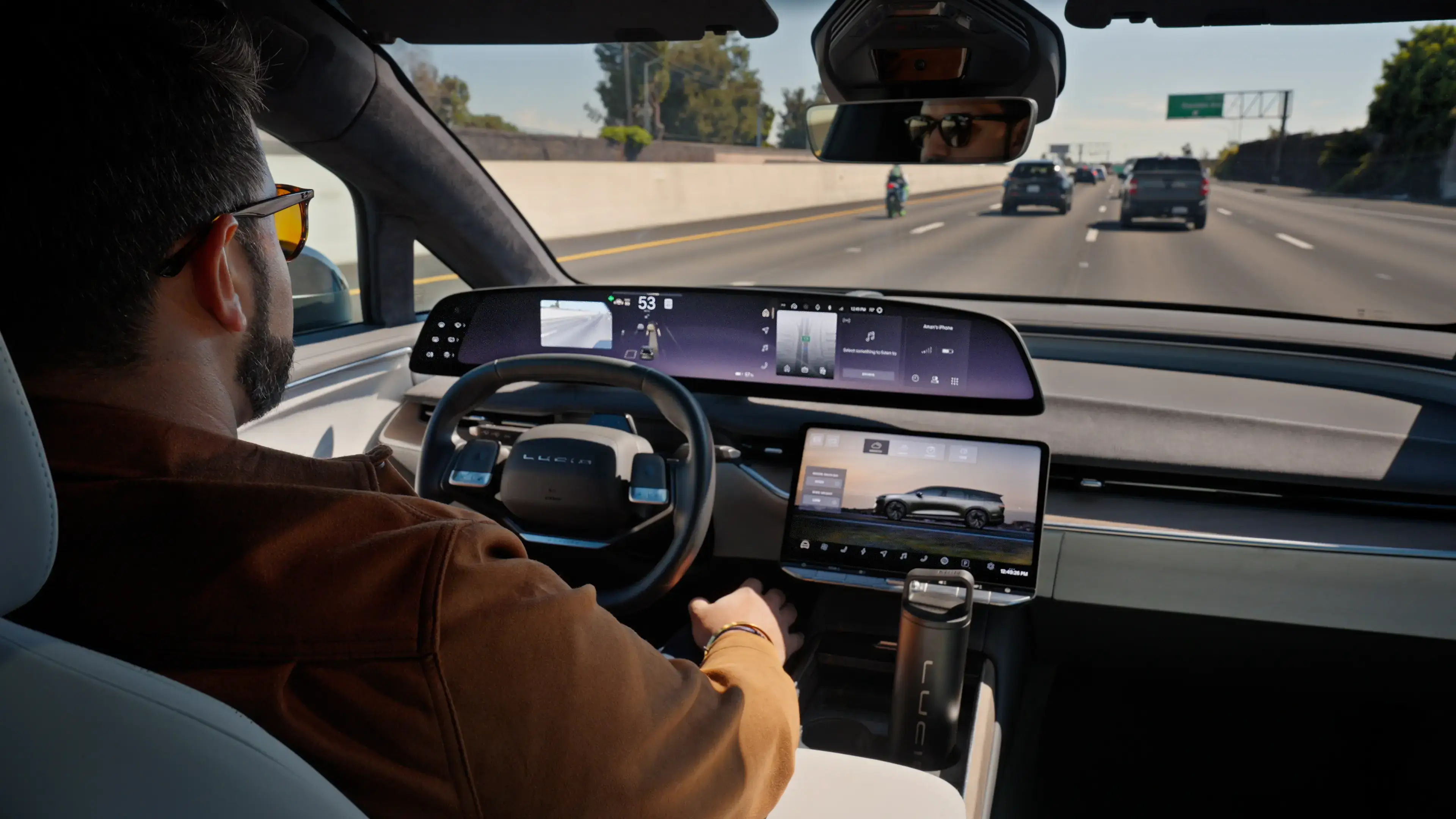 A man driving a Lucid electric vehicle on a highway, with large touchscreen displays showing navigation and vehicle info.