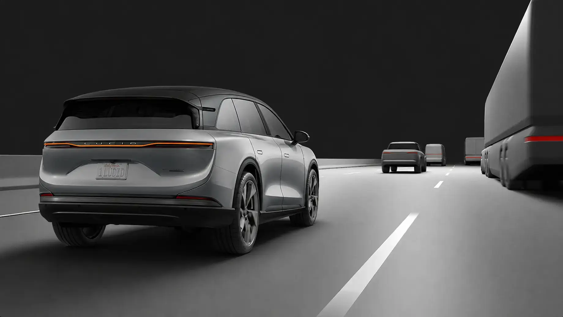 Rear view of a silver Lucid electric SUV driving on a highway at night with other vehicles nearby.