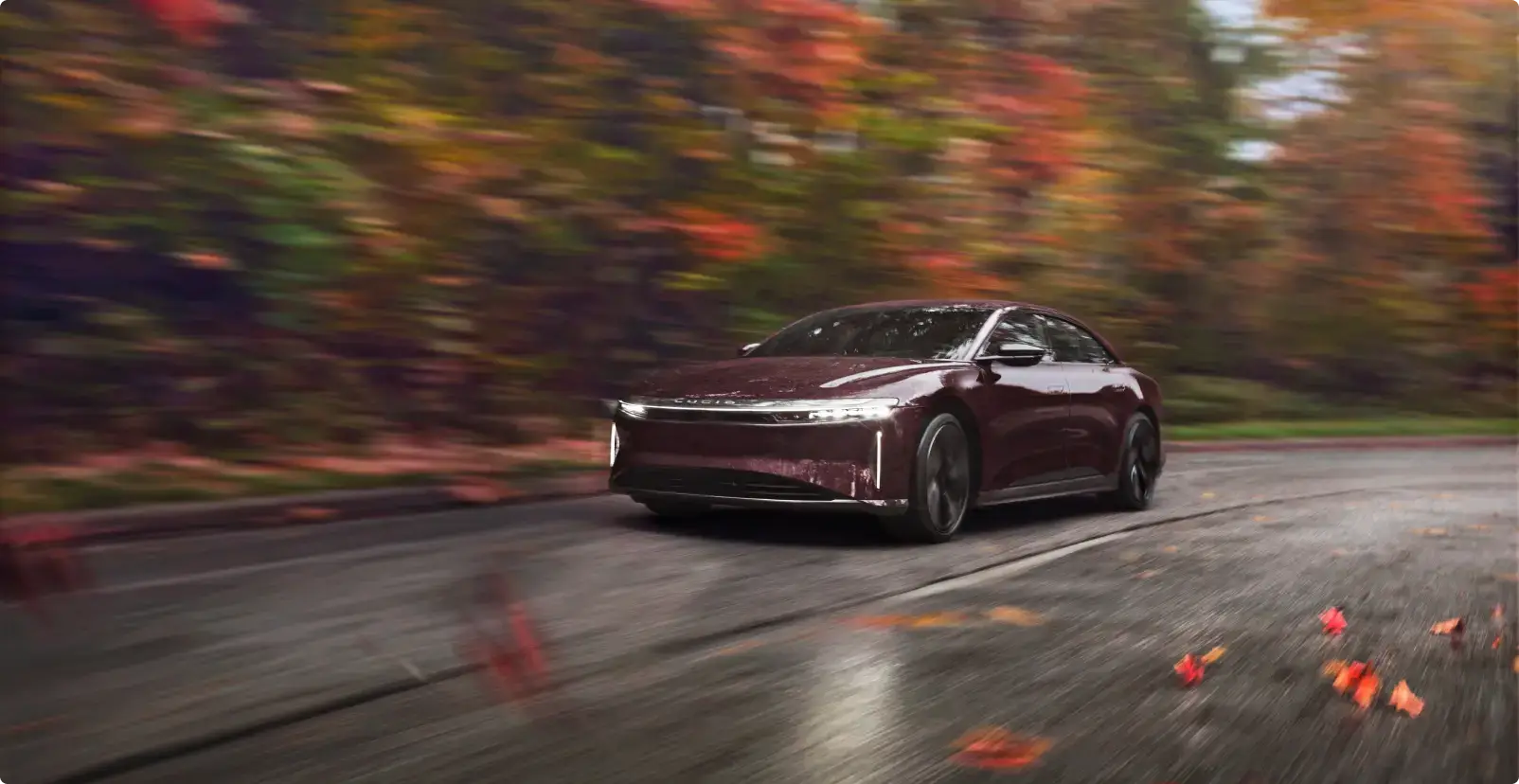 Lucid Air driving on wet road through autumn forest with vibrant red and orange foliage.