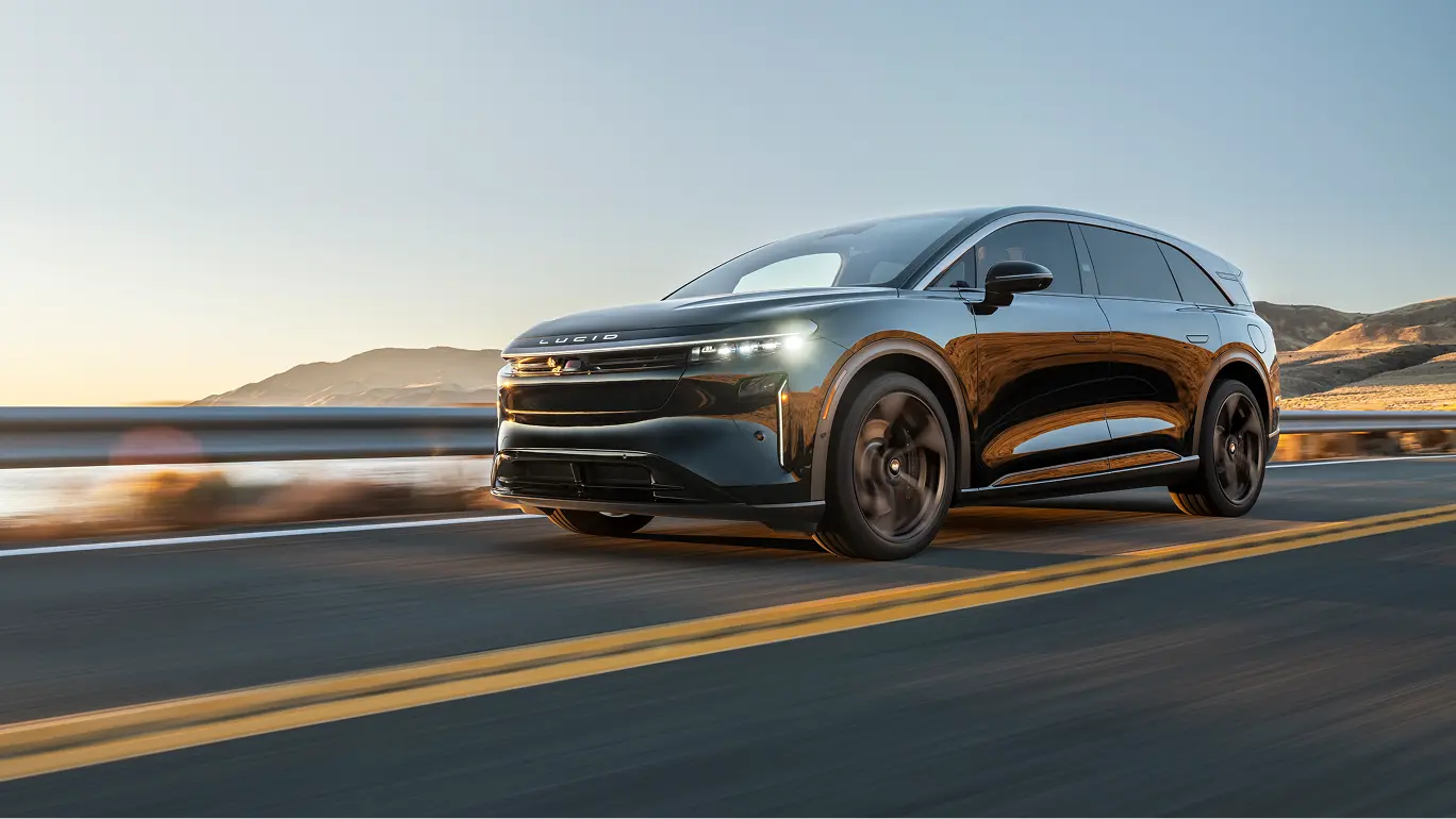 Sleek black Lucid Gravity SUV driving on coastal highway at sunset, mountains visible in background.
