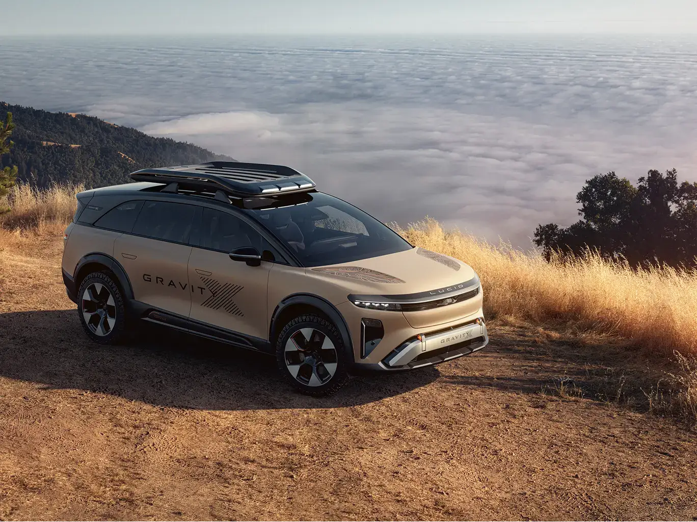 Lucid Gravity electric SUV parked on a mountain trail above a sea of clouds, with roof rack and beige exterior.