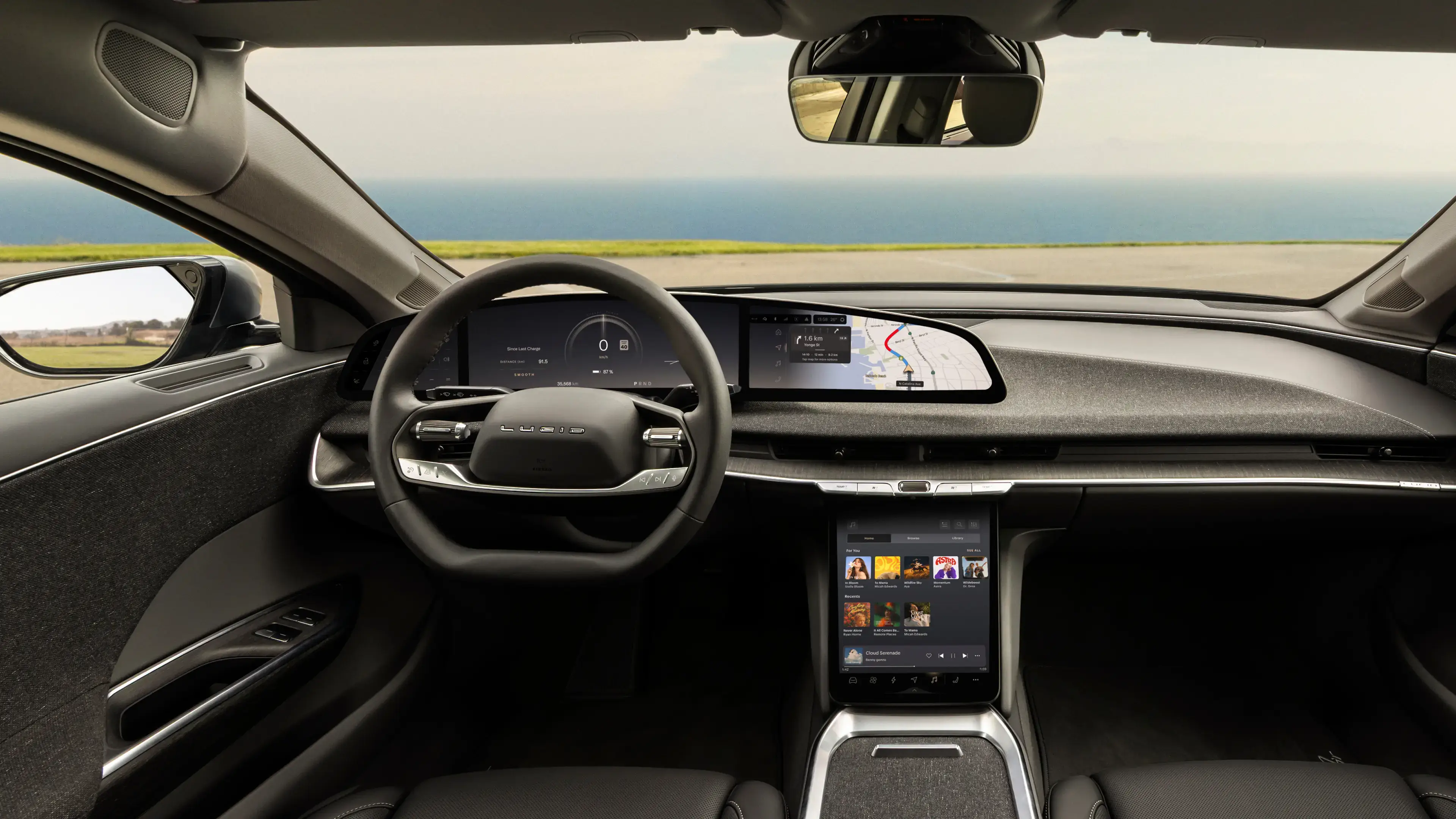 Intérieur de voiture électrique Lucid avec volant, large tableau de bord numérique, affichage de navigation et écran tactile central affichant de la musique.