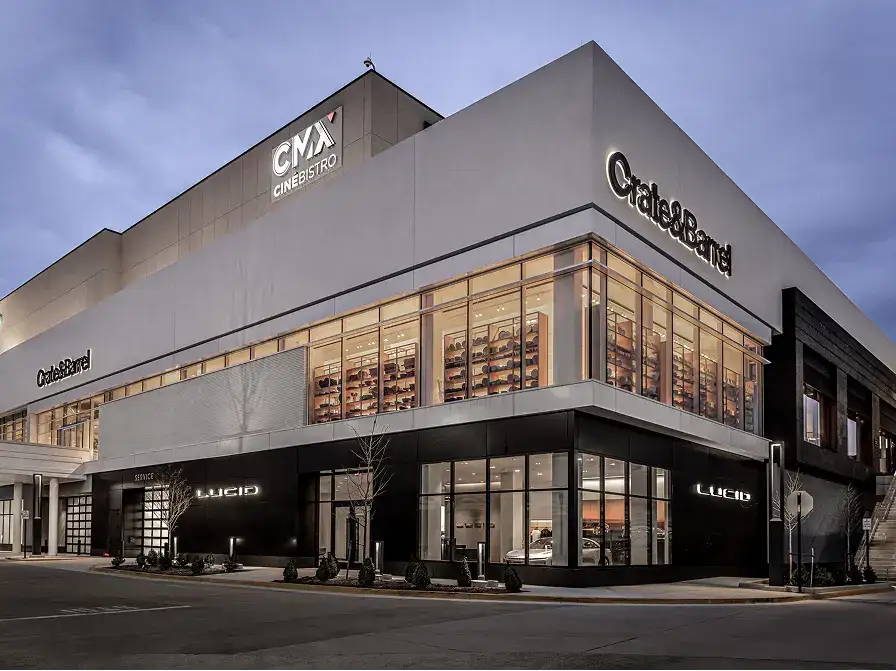 Exterior of a shopping complex at dusk featuring CMX CinéBistro, Crate & Barrel, and a Lucid Motors showroom.