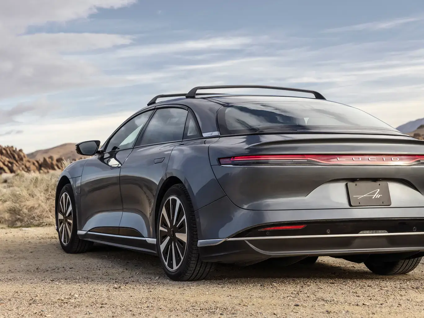 Lucid Air stationnée dans un paysage désertique avec des montagnes et un ciel nuageux en arrière-plan.