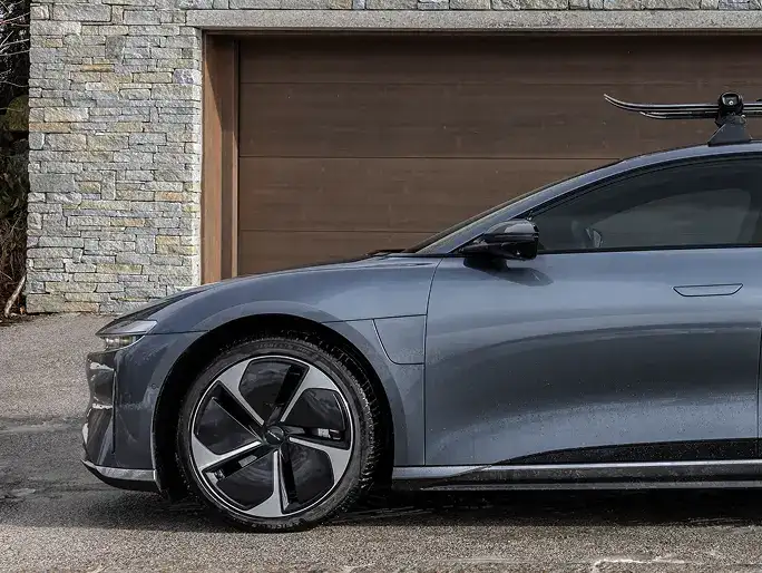 Side view of a sleek Lucid Air parked in front of a stone house with wooden garage door.