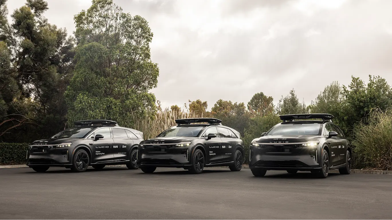 Three sleek Lucid electric vehicles parked side by side on pavement against a backdrop of trees and cloudy sky.