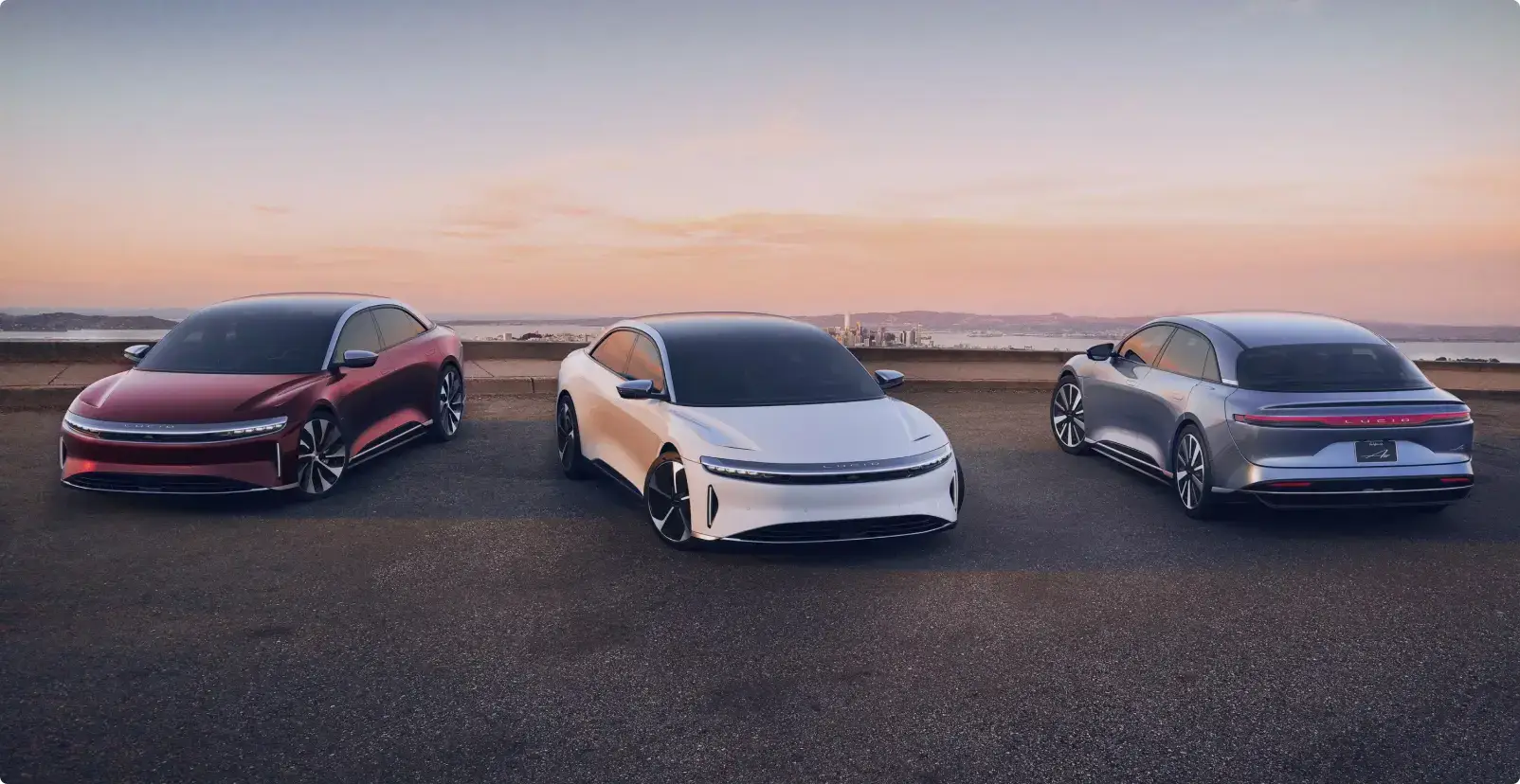 Three Lucid Air at sunset on concrete with a desert behind them in the distance.