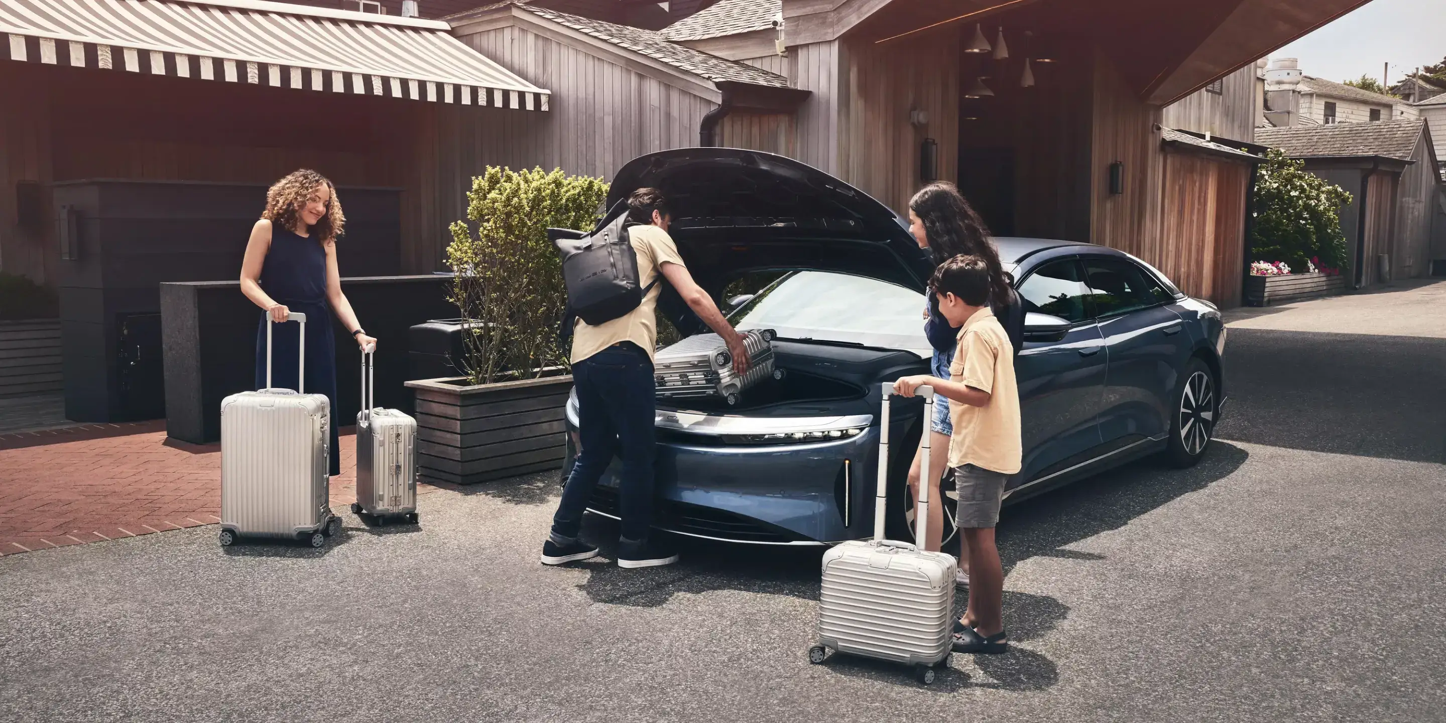 يظهر رجل وامرأة وهما يركبان سيارة Lucid Air Pure باللون الأزرق فاثوم المعدني. يقع هذا المشهد في بلدة شاطئية، مع متاجر ومظلات في الخلفية.