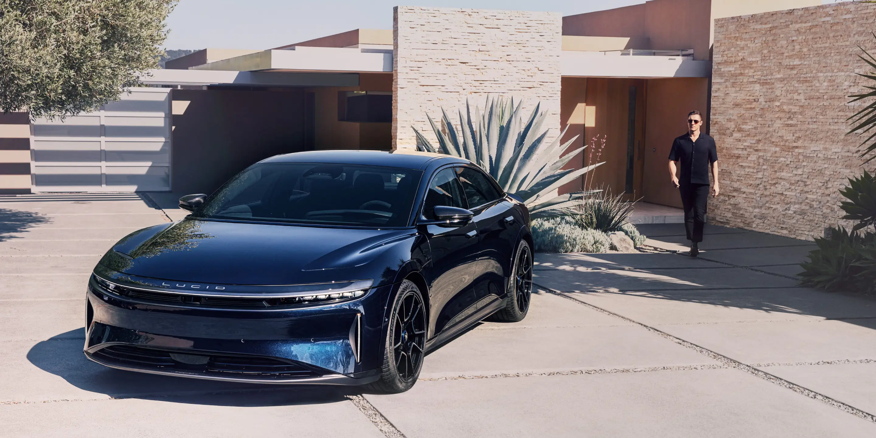 امرأة تقود سيارة Lucid Air بثقة وسعادة. وقد أُخذت الصورة من منطقة القدمين أمام مقعد الراكب الأمامي. ويمكن رؤية الجبال من خلال نوافذ السيارة خلف المرأة.