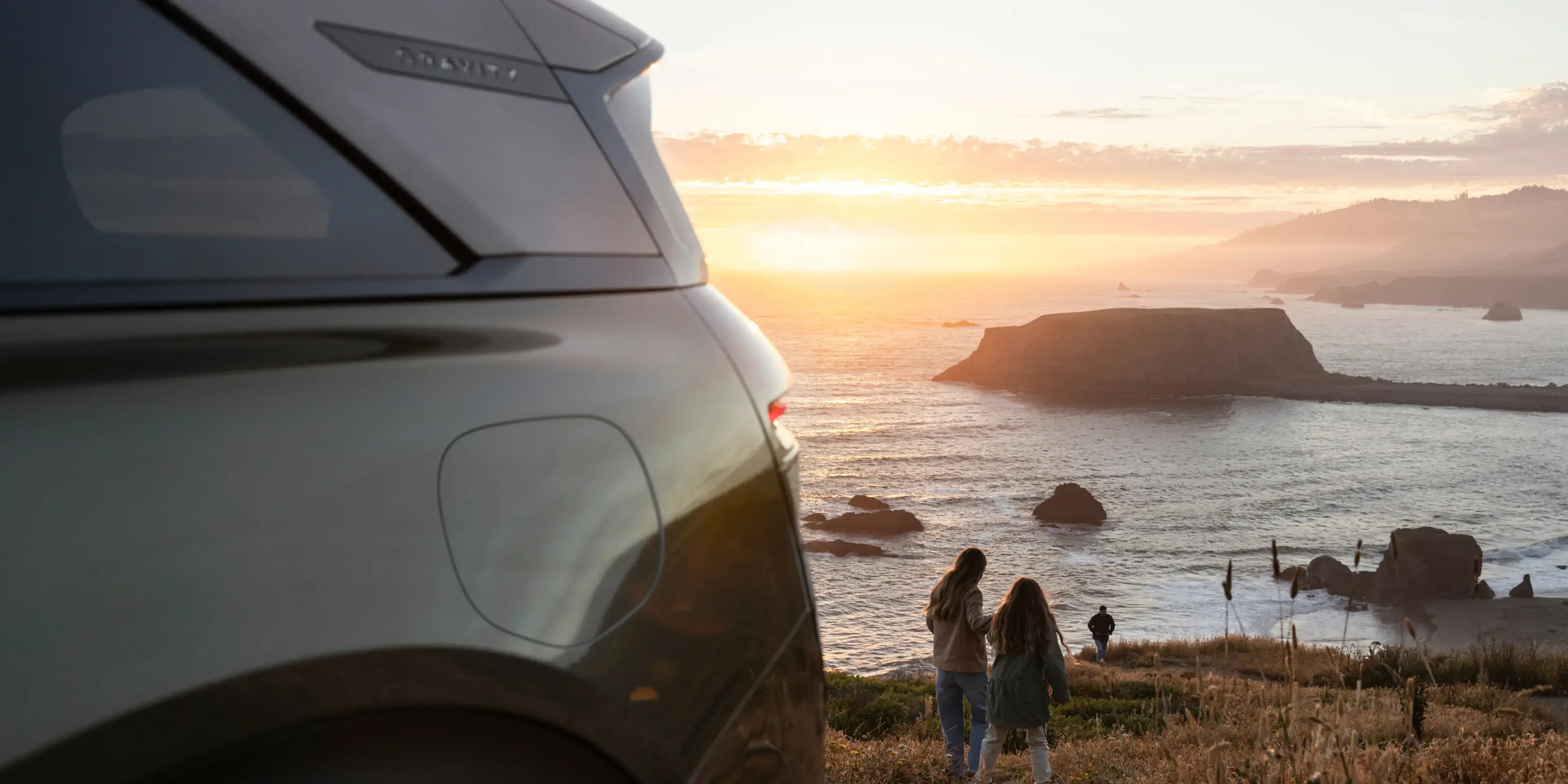 أم وابنتها تسيران بجوار سيارة Lucid Gravity باتجاه الساحل عند الغروب.