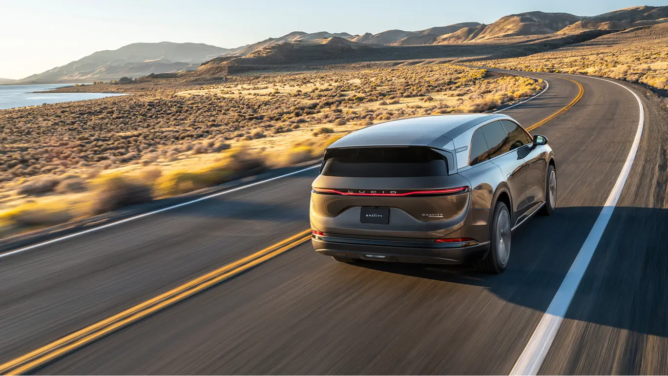 Lucid Gravity driving on a desert highway with mountains and water in the background at golden hour.