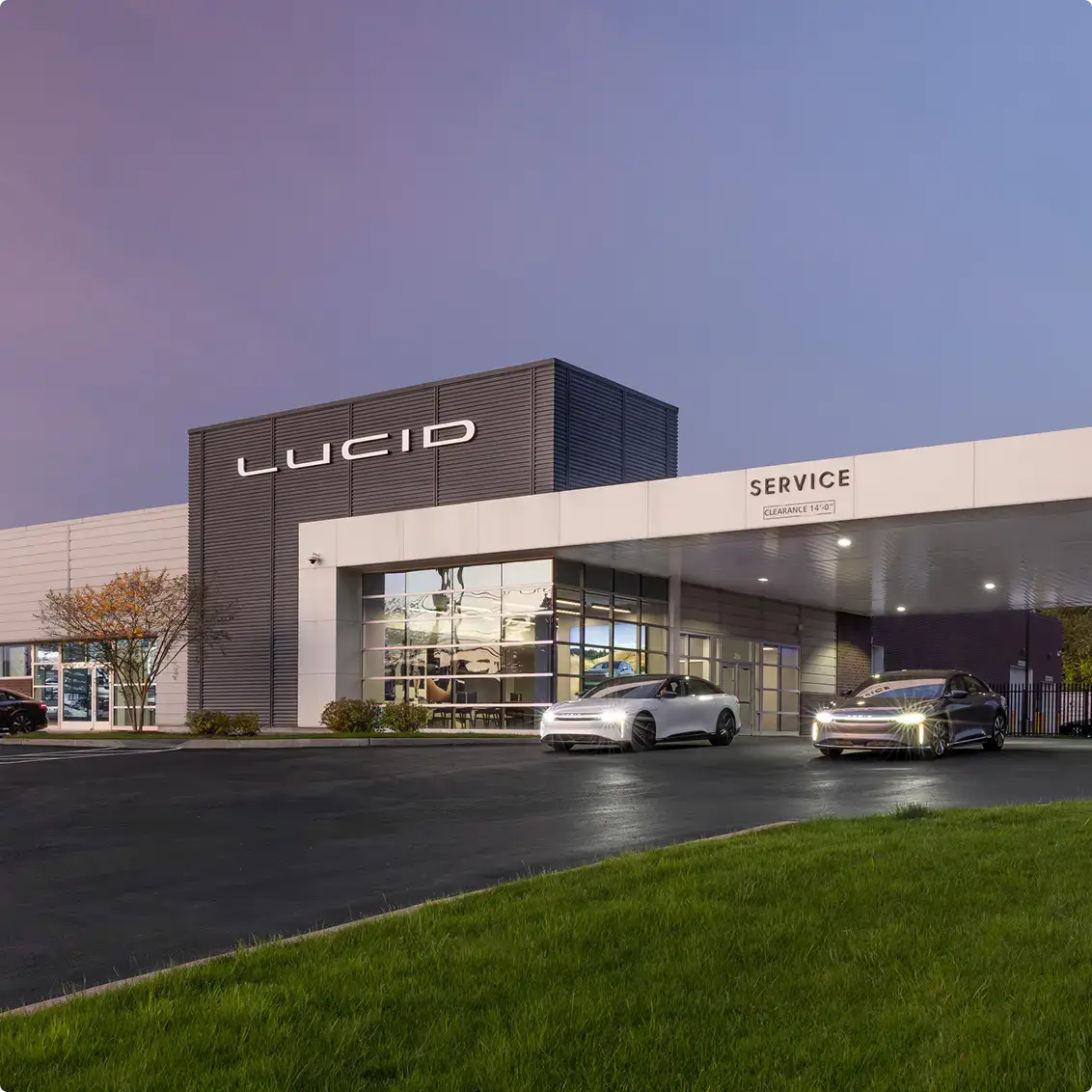 Lucid Motors service center at dusk with two electric sedans parked outside under a purple-blue sky.