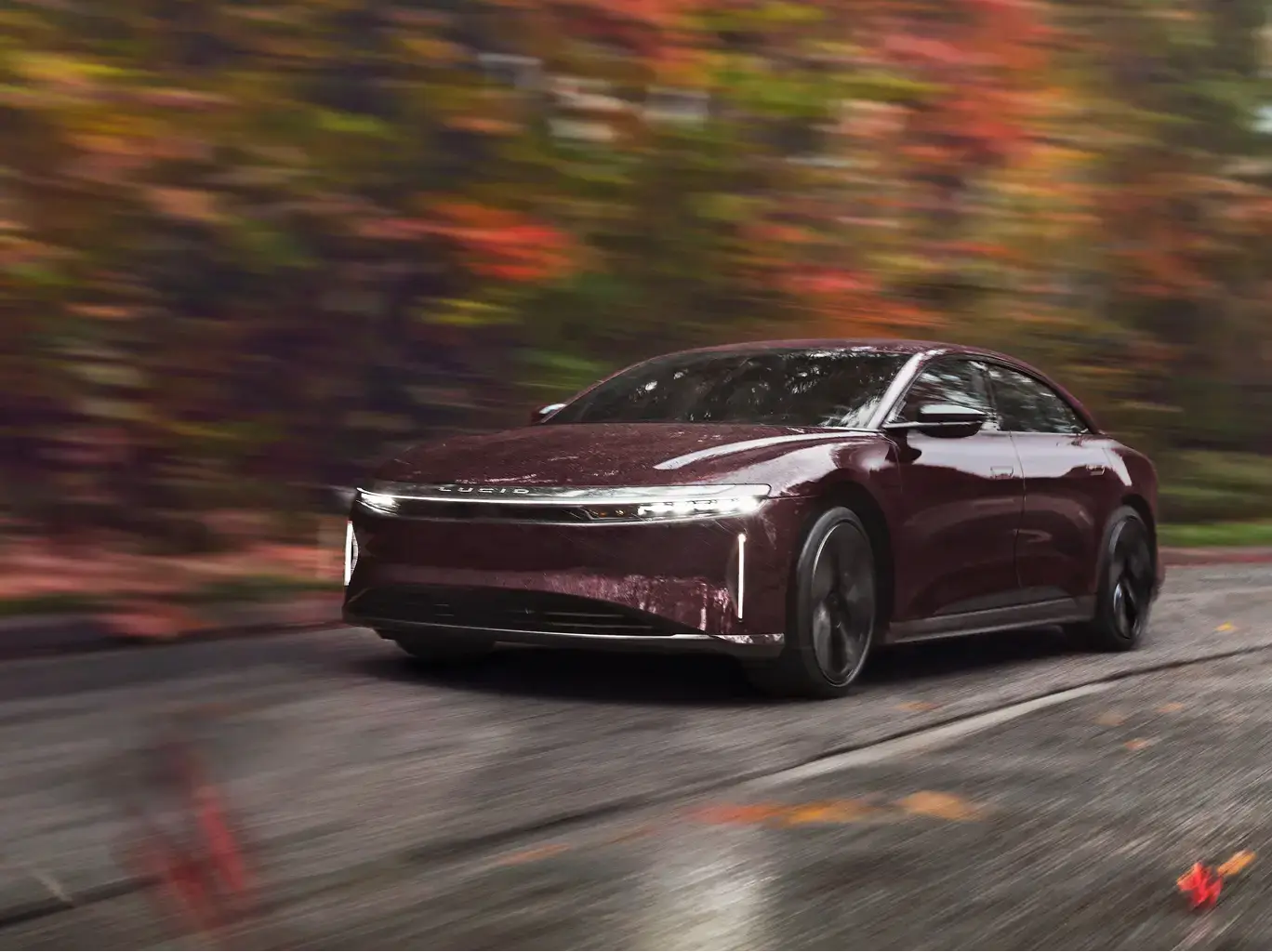 Lucid Air electric sedan driving on a road with motion-blurred autumn foliage in the background.