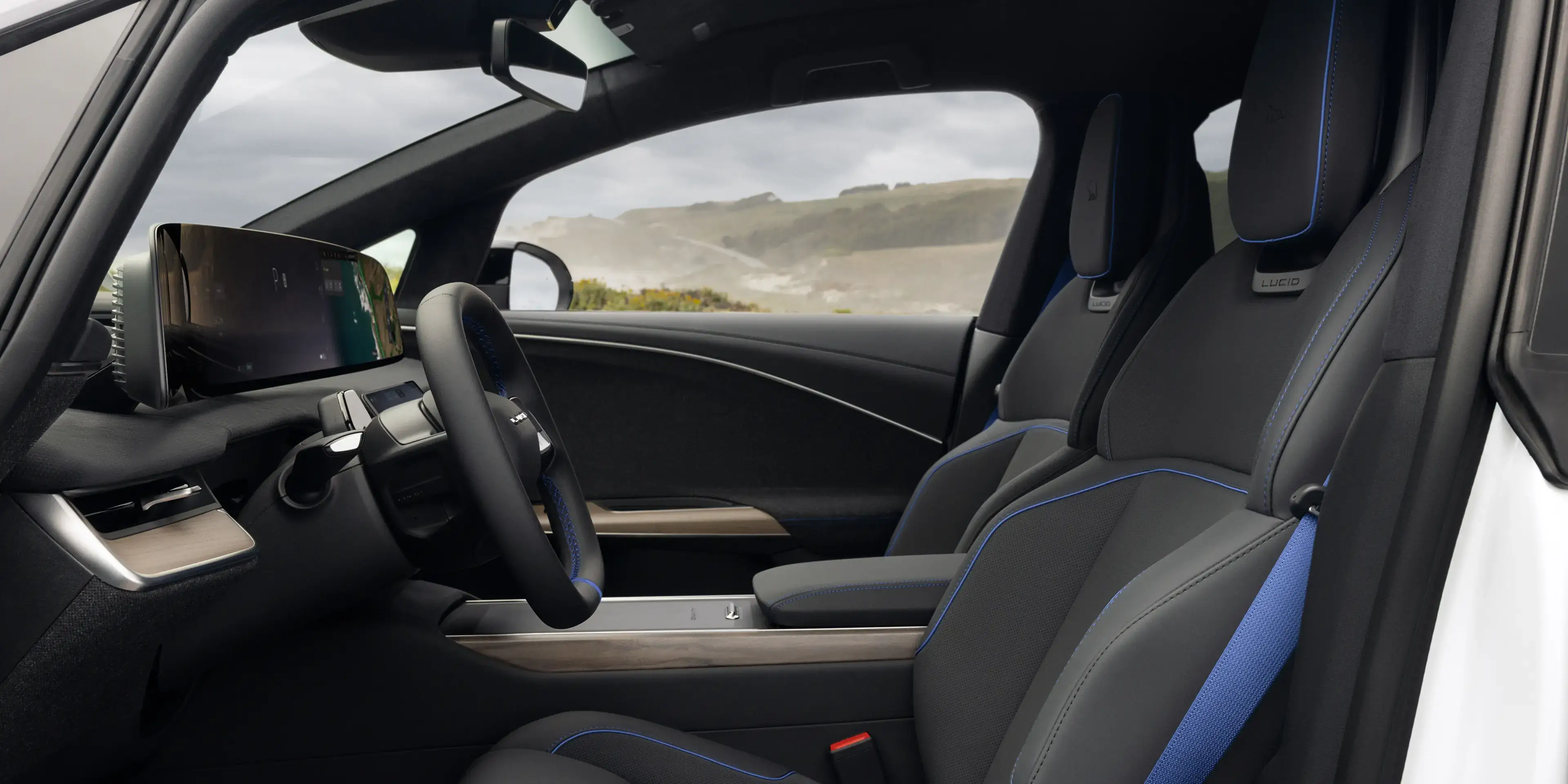 Lucid electric car interior with dark seats featuring blue accents, a yoke steering wheel, and a large touchscreen display.