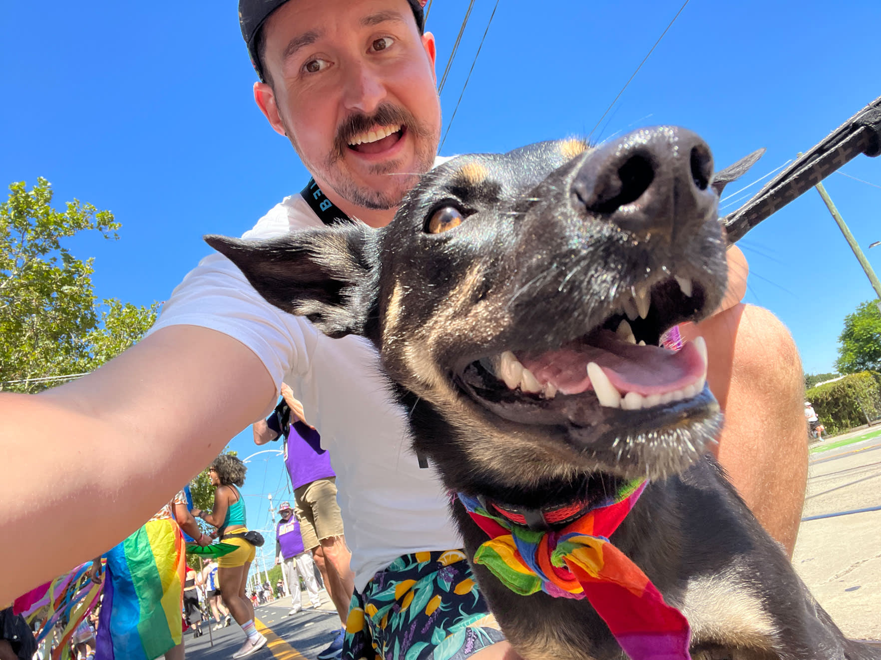 Steve from the Belong Social Team poses during Pride March with a dog wearing a rainbow scarf.