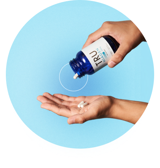 A hand is holding a Tru Niagen bottle and pouring out capsules