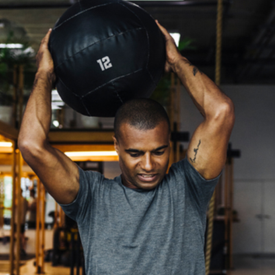 Man lifting a weighted ball over his head at the gym.