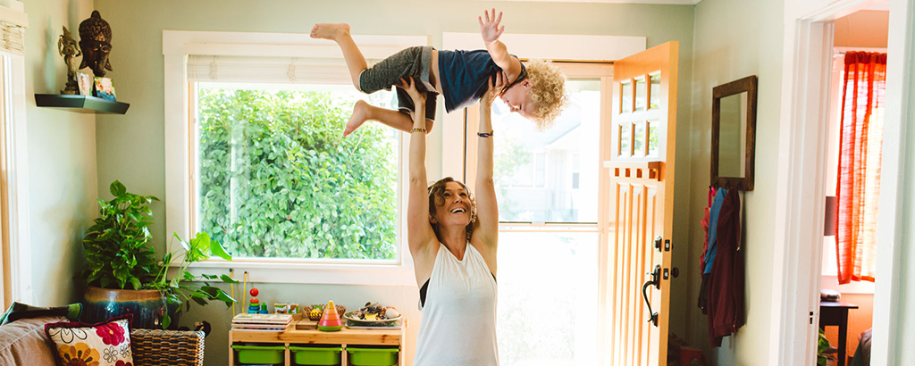 A mother carrying her young child while working out at home.