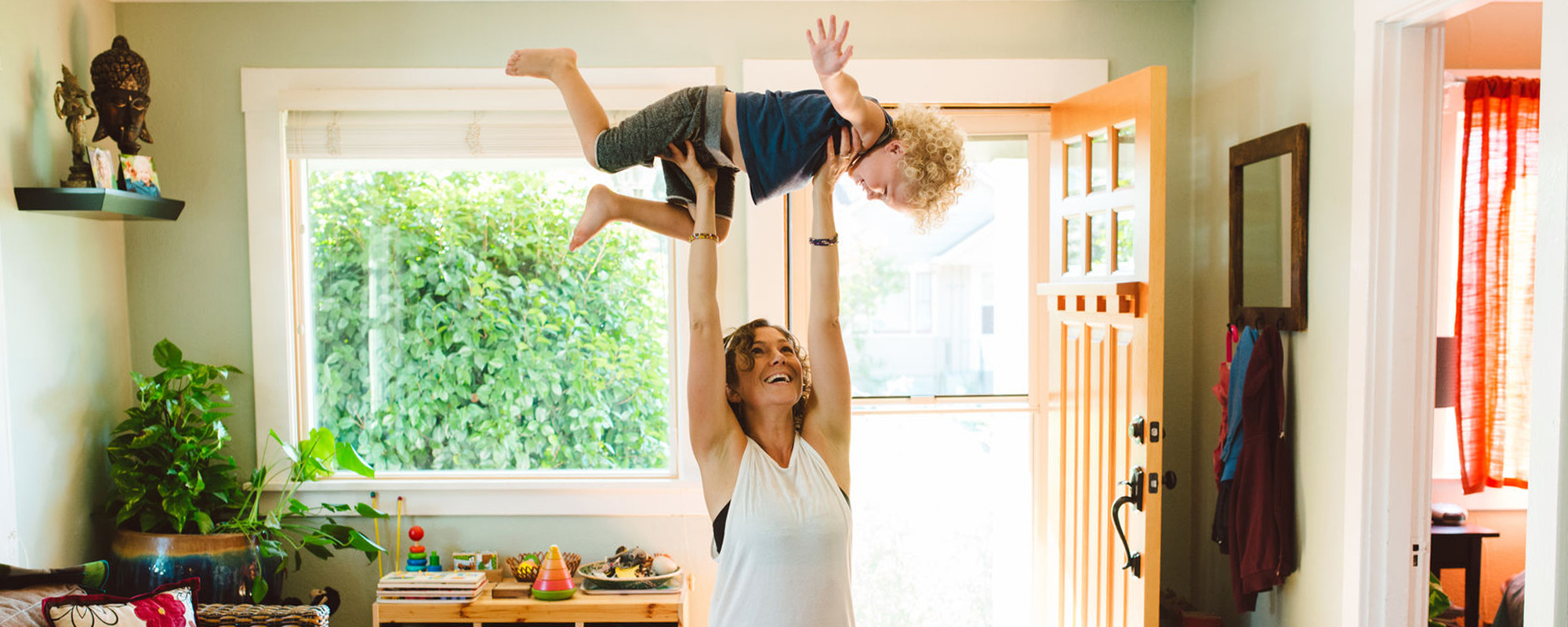 A mother carrying her young child while working out at home.