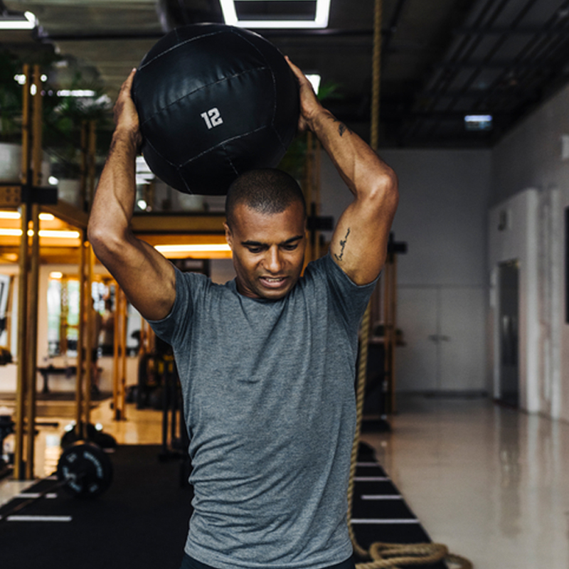 Man lifting a weighted ball over his head at the gym.