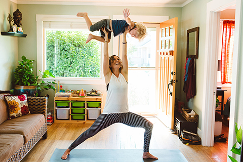 A mother carrying her young child while working out at home.