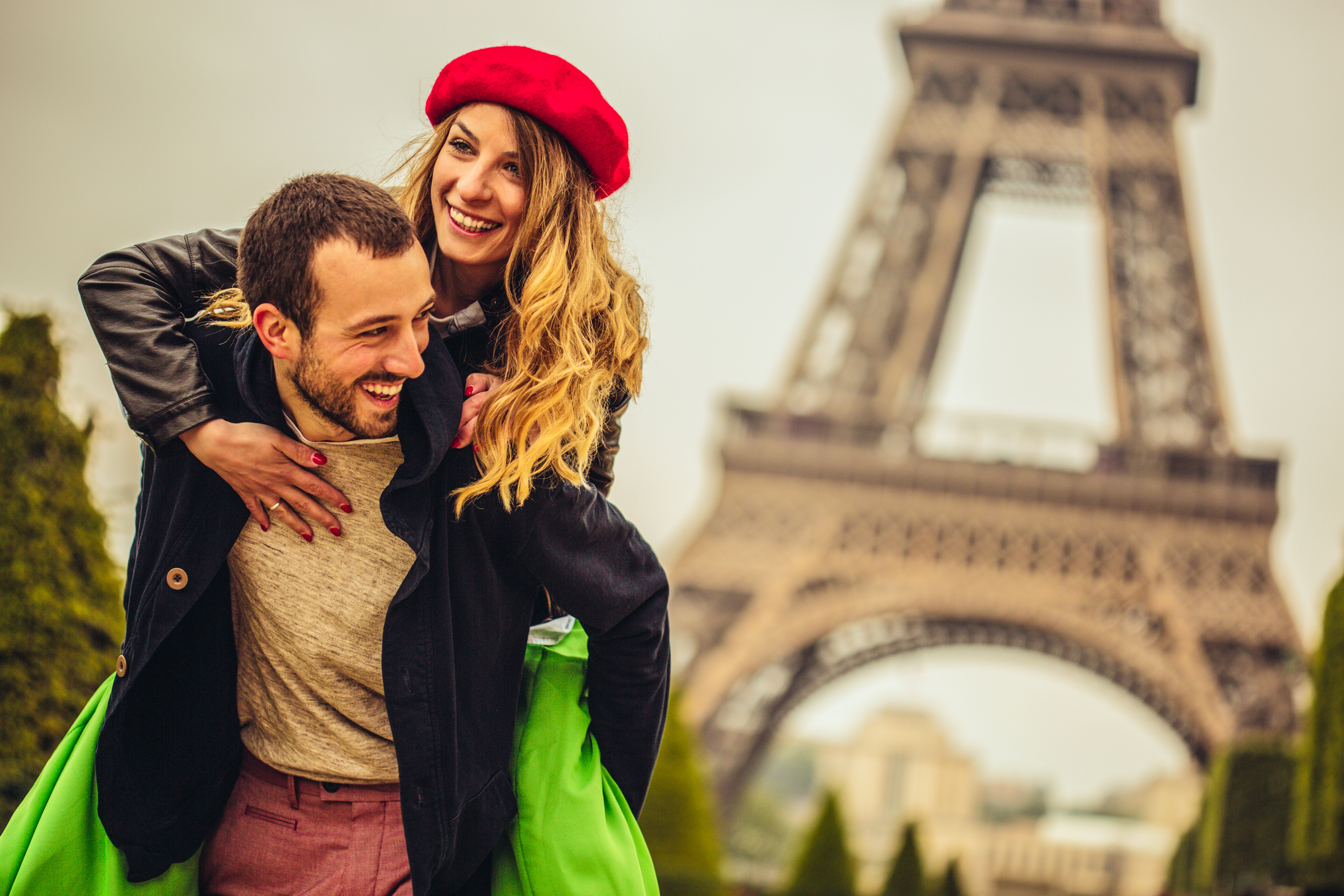 Coppia felice a Parigi, ragazza bionda con cappello francese rosso in spalle al ragazzo, sullo sfondo la Tour Eiffel