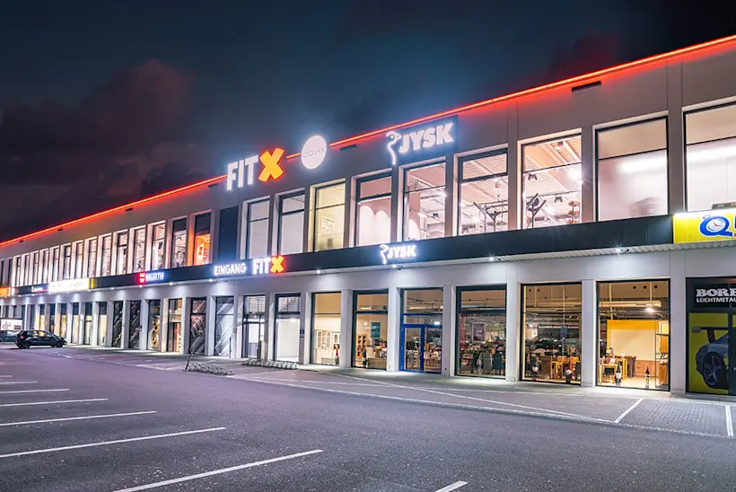 Bild: Außenansicht eines FitX Fitnessstudios. Ein großes FitX-Logo mit orangefarbenem X ist zu sehen. Das Gebäude befindet sich in einem urbanen Umfeld.