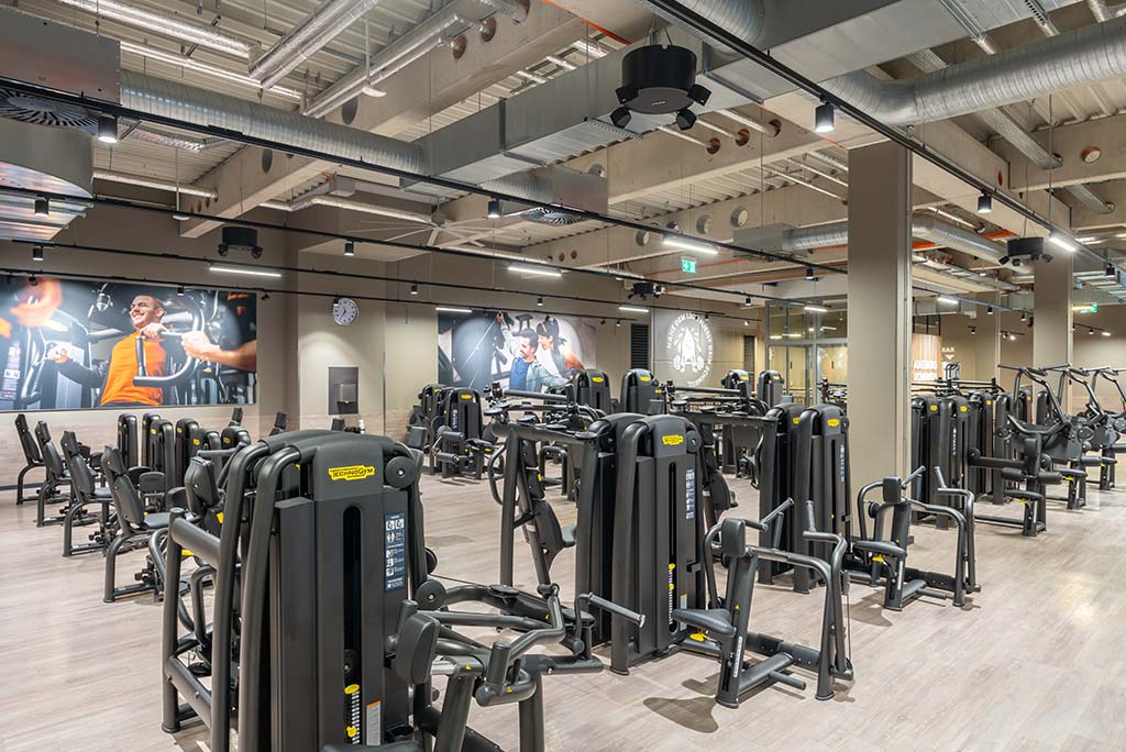 Gerätebereich im FitX Fitnessstudio Augsburg-Lechhausen mit verschiedenen Kraftgeräten. Der Raum ist im industriellen Design gestaltet, mit offenen Deckenstrukturen und hellen Böden.