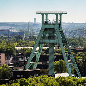 Grüner Förderturm des Deutschen Bergbau-Museums Bochum, umgeben von Bäumen und Stadtlandschaft im Hintergrund.