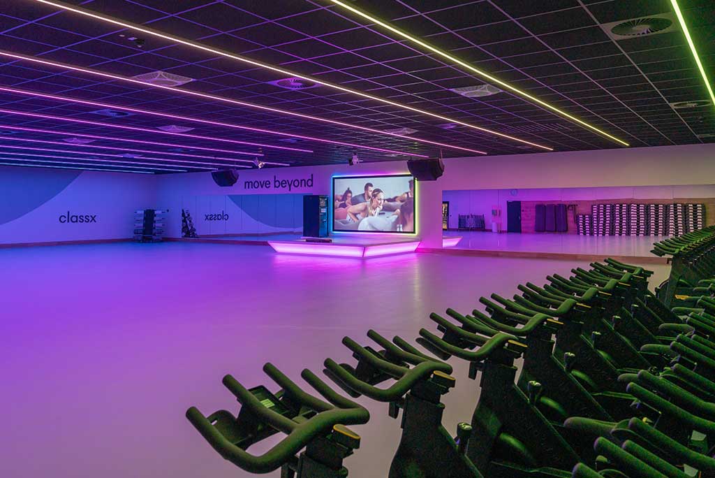Großer, offener Kursraum im FitX Fitnessstudio Nürnberg-Zabo. An der hinteren Wand befindet sich eine erhöhte Bühne, dahinter eine Leinwand. Links und rechts davon sind Spiegelwände.