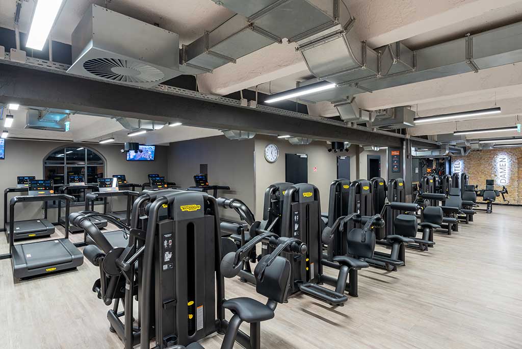 Gerätebereich im FitX Fitnessstudio Berlin-Moabit mit verschiedenen Kraftgeräten. Der Raum ist im industriellen Design gestaltet, mit offenen Deckenstrukturen und hellen Böden.