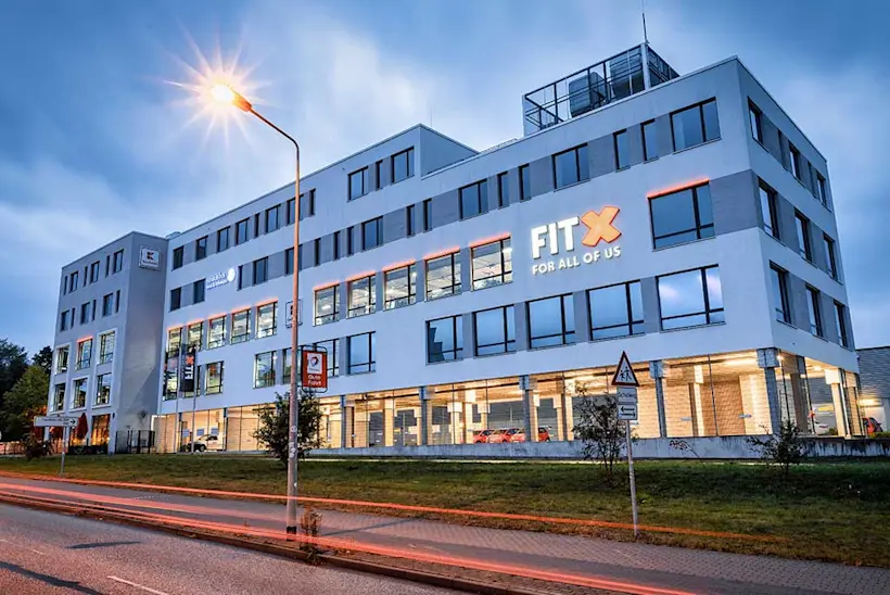 Bild: Außenansicht eines FitX Fitnessstudios. Ein großes FitX-Logo mit orangefarbenem X ist zu sehen. Das Gebäude befindet sich in einem urbanen Umfeld.