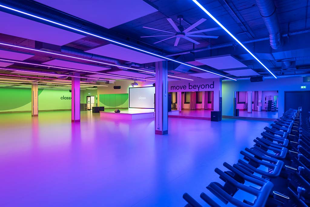 Großer, offener Kursraum im FitX Fitnessstudio Essen-Bergerhausen. An der hinteren Wand befindet sich eine erhöhte Bühne, dahinter eine Leinwand. Links und rechts davon sind Spiegelwände.