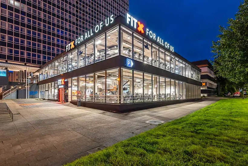 Bild: Außenansicht eines FitX Fitnessstudios. Ein großes FitX-Logo mit orangefarbenem X ist zu sehen. Das Gebäude befindet sich in einem urbanen Umfeld.