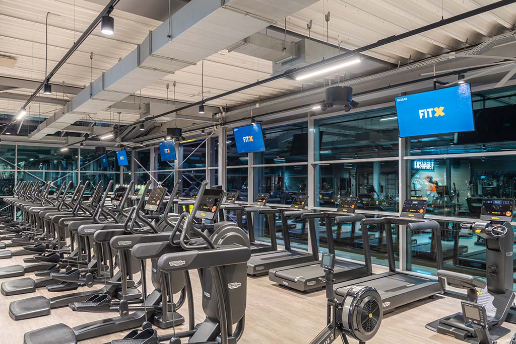 Offener Bereich für Ausdauertraining im FitX Fitnessstudio Neuss-Innenstadt mit verschiedenen Cardio-Geräten. An den Wänden hängen Fernseher.
