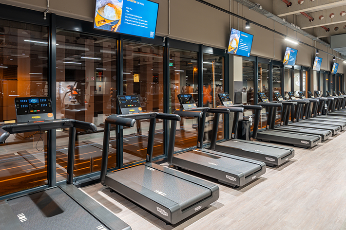 Zirkel-Bereich im FitX Fitnessstudio Augsburg-Lechhausen, in dem verschiedene Trainingsgeräte kreisförmig angeordnet sind. Über den Geräten hängt ein großer Leuchtring, der in grün oder rot leuchtet und die Übungsdauer anzeigt.