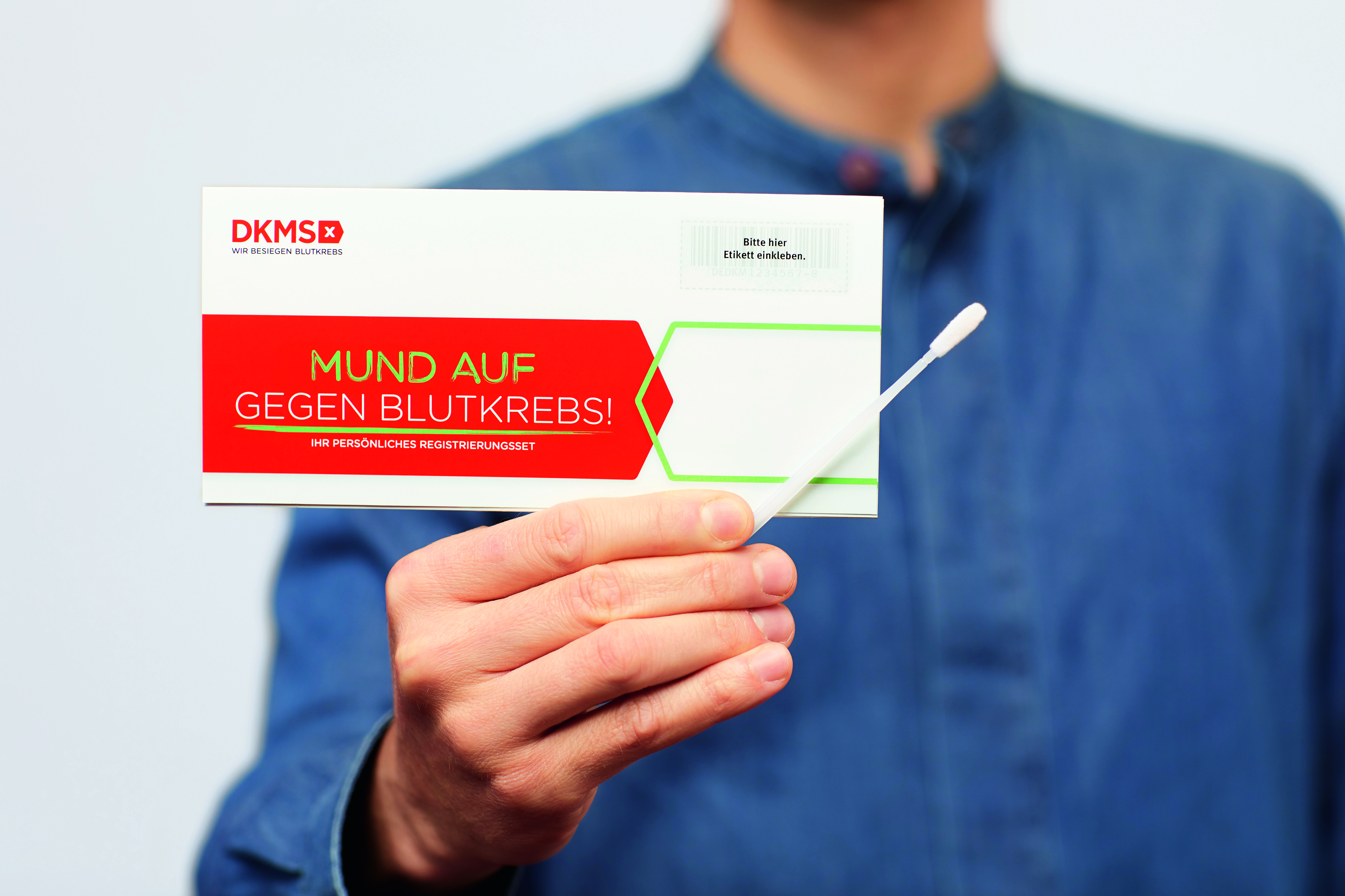 Bild: Bild einer Person, die ein Registrierungsset zur Stammzellenspende und ein langes Wattestäbchen in der Hand hält.